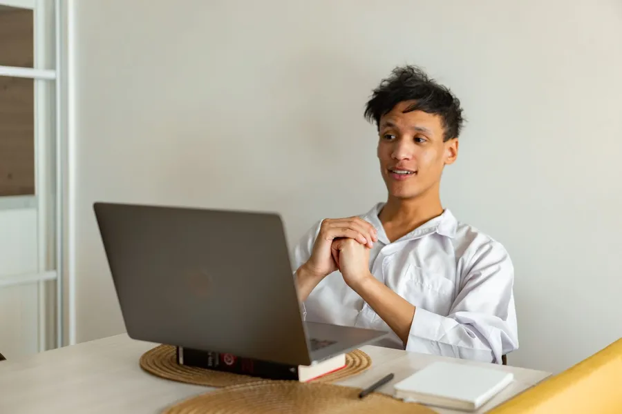 A young man following an online class on a laptop at home