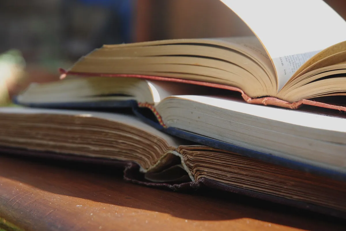 A stack of open books on a sunlit wooden table