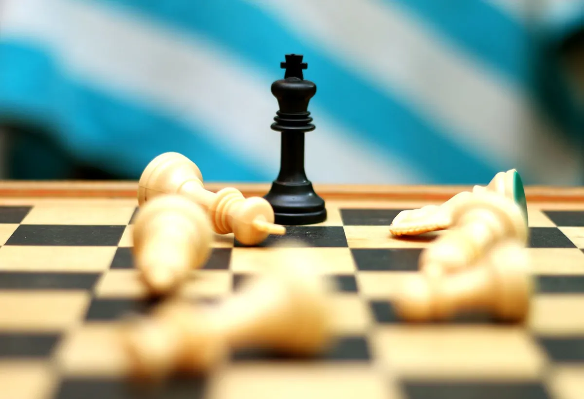 A black king chess piece standing on a board among fallen white pieces