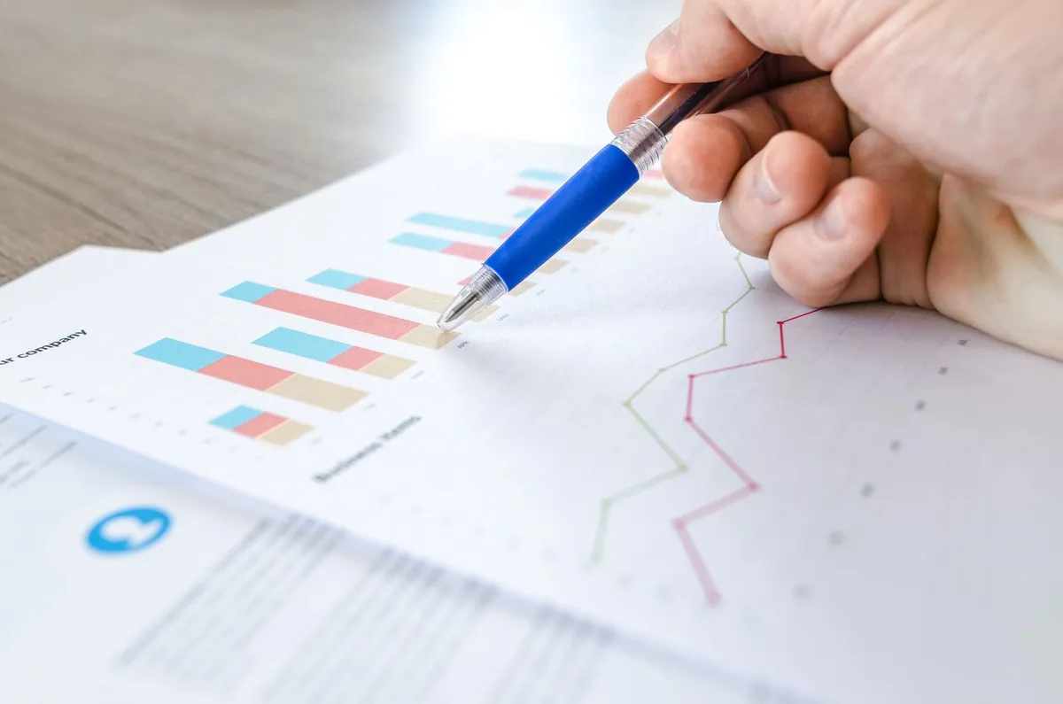 A hand holding a pen over printed bar and line charts on paper