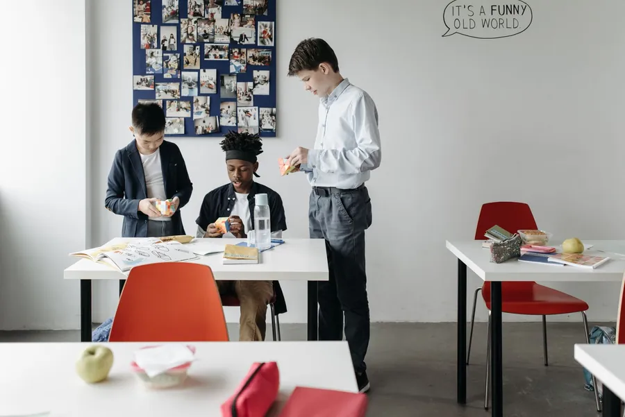 Three students in a classroom, each solving a Rubik's cube puzzle